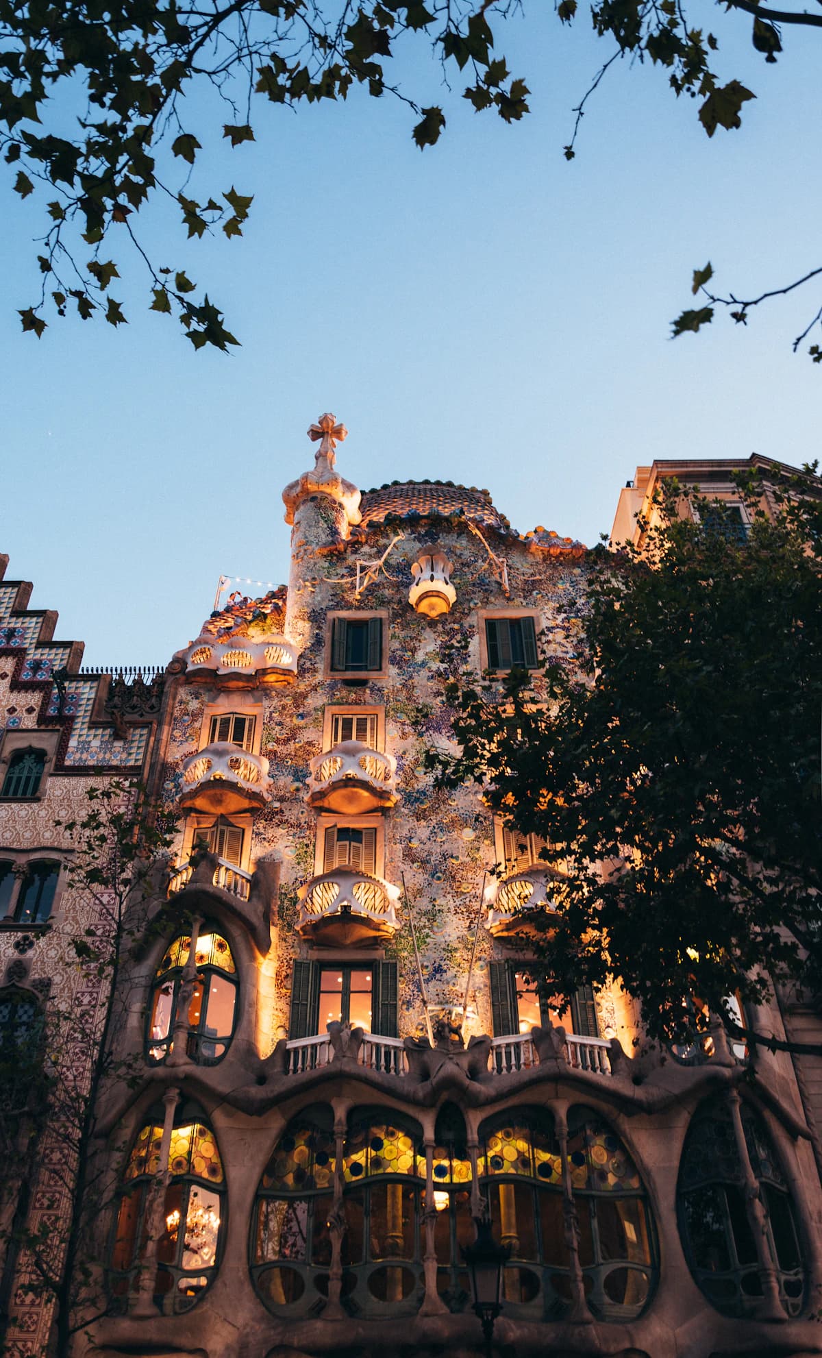 Fachada iluminada de Casa Batlló bajo los árboles en Barcelona